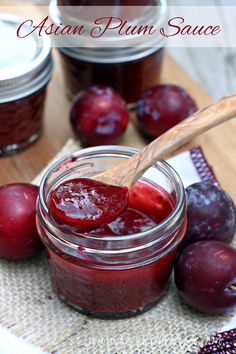 plum jam in a glass jar with a wooden spoon next to some plums on the table