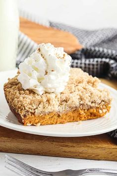 a piece of pie with whipped cream on top sitting on a white plate next to a glass of milk