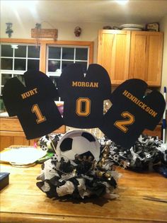 a table topped with black and gold decorations in the shape of heart shaped numbers, soccer balls and tassels