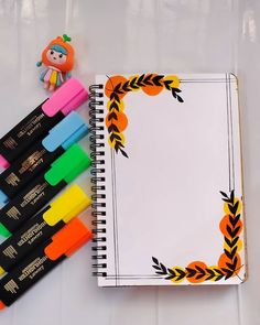 an open notebook with markers and a doll next to it