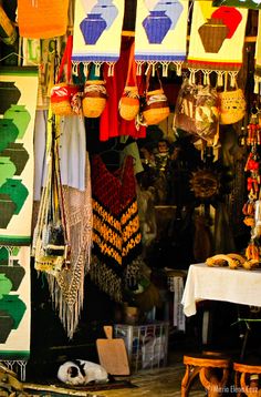 there are many colorful items hanging from the ceiling in this market place, including hats and rugs