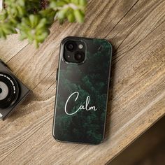 a phone case with the word calm on it sitting next to a camera and plant