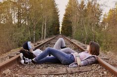 two young women laying on train tracks in the middle of an open area with trees