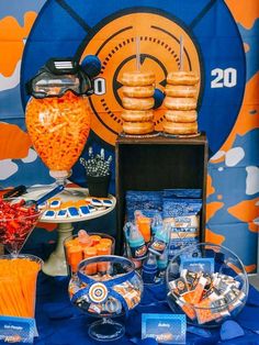 an orange and blue dessert table with donuts, candy, and drinks on it