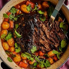 a pot filled with meat and vegetables on top of a purple table cloth next to a knife