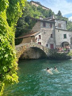 people are swimming in the water near an old stone building with a bridge over it