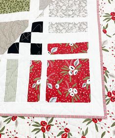 a quilted table topper with red and white flowers on the border, along with black and grey squares