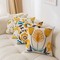 four decorative pillows on a white couch in a living room with yellow and blue flowers