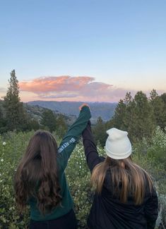 two women holding hands while standing on top of a hill