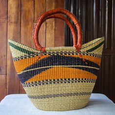 Working with Ghanaian artisans Adams Salley presents this beautiful hand woven basket tote. The raffia basket is accented with patterns in violet orange and green and finished with sturdy leather-wrapped handles. The tote is ideal for shopping or the beach or simply enjoy its beauty as a home decor accent. Brown Basket Beach Bag With Rolled Handles, Multicolor Straw Bucket Bag, Handwoven Brown Basket Beach Bag, Orange Woven Beach Bag For Shopping, Orange Beach Bag With Braided Handles For Shopping, Brown Handwoven Basket Beach Bag, Orange Woven Straw Bag For Daily Use, Orange Straw Tote Bag For Shopping, Multicolor Straw Bag With Leather Handles