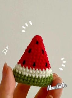 a hand is holding a small crocheted watermelon slice