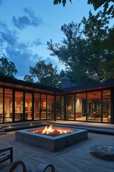 an outdoor fire pit in the middle of a courtyard at night with large windows and trees