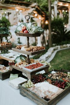 an assortment of food is displayed in wooden trays on a white table cloth outside