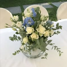 a vase filled with white and blue flowers on top of a table next to chairs