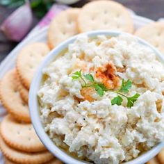 a white bowl filled with cheese and crackers on top of a table next to flowers