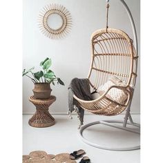 a rattan swing chair with cushions and pillows on the floor next to a potted plant