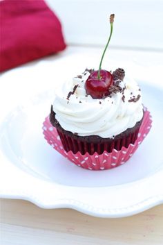 there is a cupcake with white frosting and a cherry on top, sitting on a plate