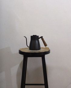 a black coffee pot sitting on top of a wooden stool next to a white wall