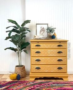 a yellow dresser sitting next to a potted plant on top of a wooden floor