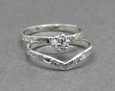 two silver rings with a diamond in the center on a gray surface, one has an engraved band