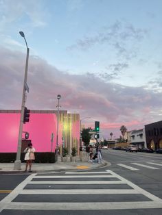 people crossing the street in front of a pink building with palm trees on both sides