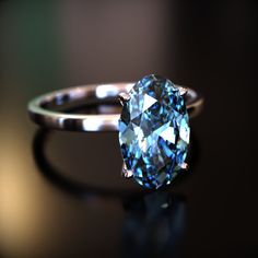 a blue diamond ring sitting on top of a black table next to a dark background