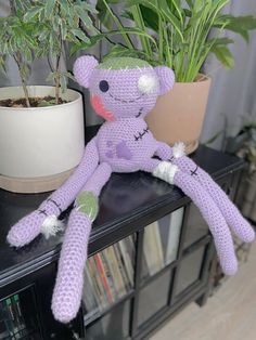 a crocheted monkey sitting on top of a table next to a potted plant