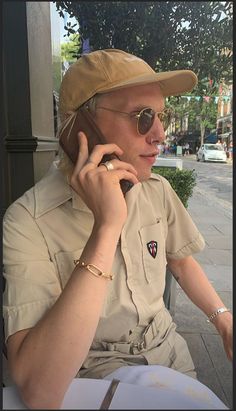 a man sitting at a table talking on a cell phone while wearing sunglasses and a hat