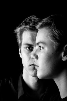 black and white photograph of two young men looking at each other's eyes in the dark