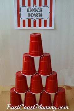 a stack of red plastic cups sitting on top of a wooden table next to a sign that says knock down