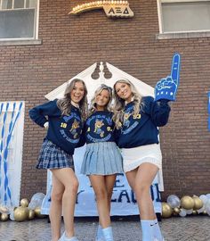 three girls are standing in front of a building and posing for the camera with their hands up