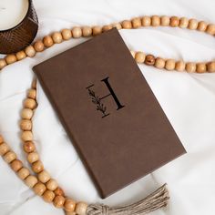 a wooden rosary with a brown bible on it next to a candle and a beaded necklace