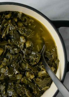 a pot filled with green vegetables on top of a stove next to a silver spoon