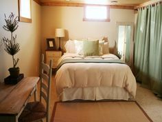 a bed sitting next to a wooden table in a room with green drapes on the windows