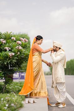 a man and woman standing next to each other on a sidewalk near flowers in the background