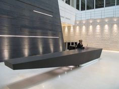 a woman is sitting at a desk in an office building with lights on the walls