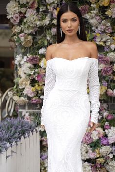 a woman in a white wedding dress standing next to a flower covered wall with flowers