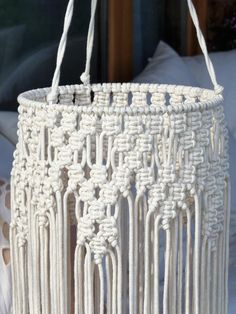 a white macrame bag hanging from a hook on a bed with pillows in the background