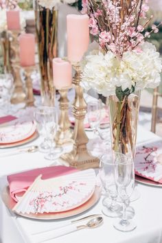 the table is set with pink and white flowers in vases, candles, and napkins