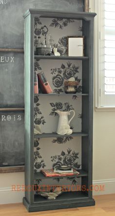 an old bookcase is painted with black and white floral wallpaper, along with a chalkboard background