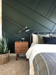 a bedroom with dark green walls and white bedding, two plants on the nightstand