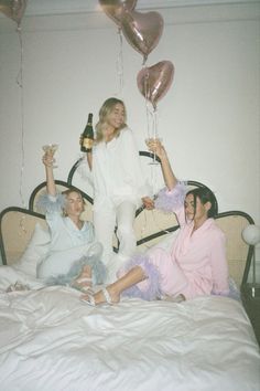 two women and one man sitting on a bed with balloons in the shape of hearts