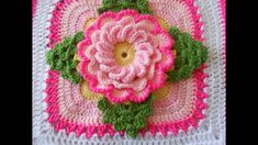 a crocheted square with a pink flower on the center and green leaves in the middle