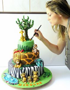 a woman is writing on the top of a giraffe cake with other animals