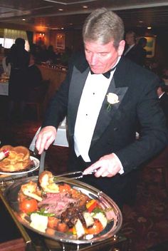 a man in a tuxedo cutting into a platter with food on it