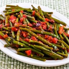 a white plate topped with green beans covered in tomato sauce and seasoning next to a fork