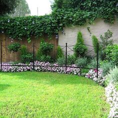 a fenced in garden with pink flowers and greenery on the side of it