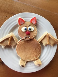 a white plate topped with pancakes covered in icing and decorated like a bat, on top of a wooden table