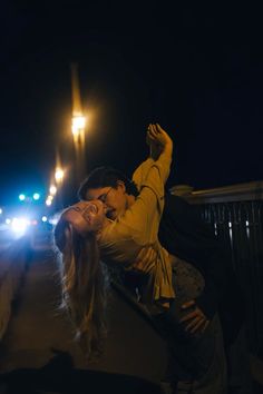 a man and woman kissing in the street at night with their arms around each other