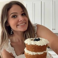 a woman sitting in front of a cake with blueberries and cream frosting on it